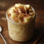 A jar of creamy overnight oats topped with diced apples and a sprinkle of cinnamon, with a spoon on the side.