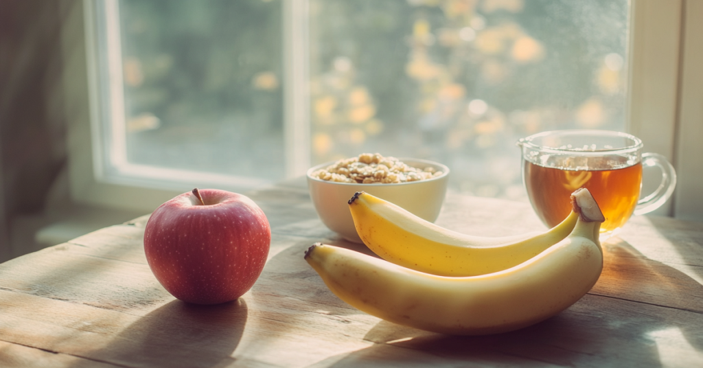 Banana, apple, a bowl of granola, and a cup of tea on a wooden surface near a window.